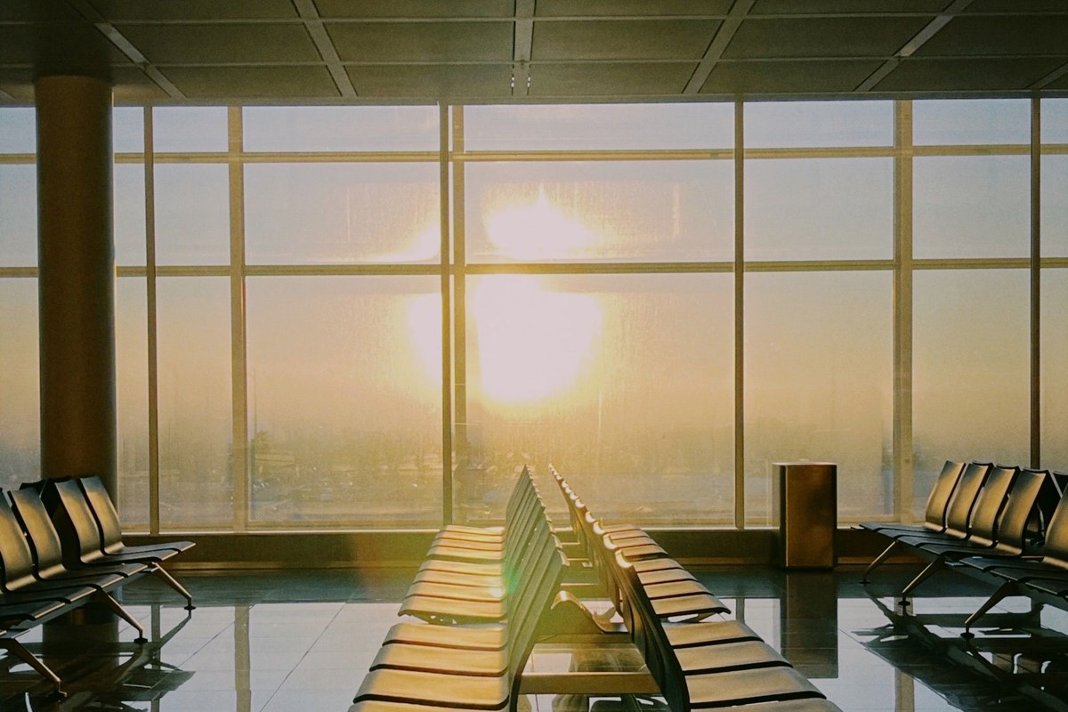 An empty airport terminal at sunrise, rows of seats and light through the windows