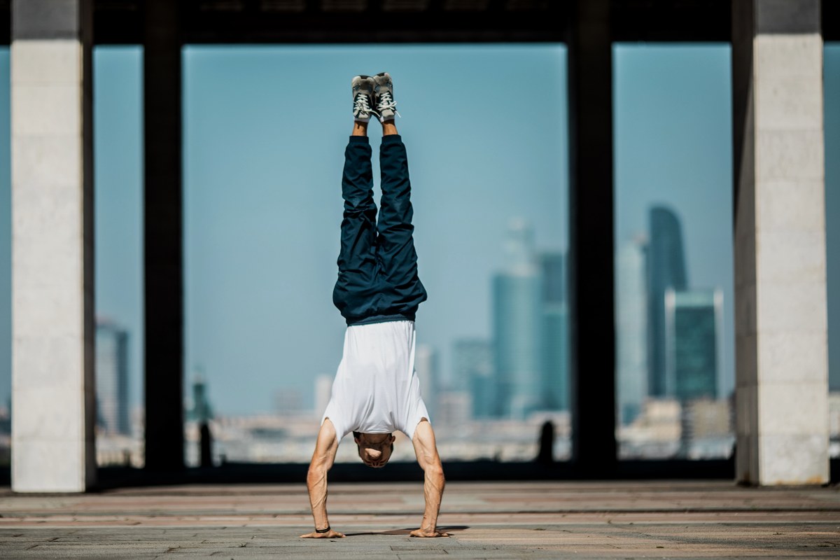 A fit man doing a handstand on a rooftop with a city skyline behind him
