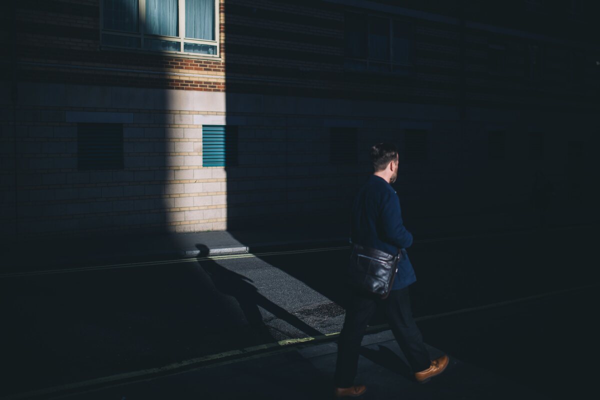 A person walking through light and shadow on a quiet street